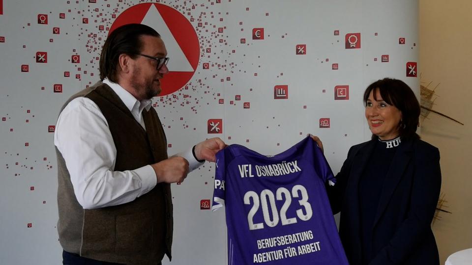 Dr. Michael Welling, Geschäftsführer des VFL Osnabrück und Christiane Fern, Leiterin der Osnabrücker Agentur für Arbeit halten gemeinsam ein VFL Trikot hoch