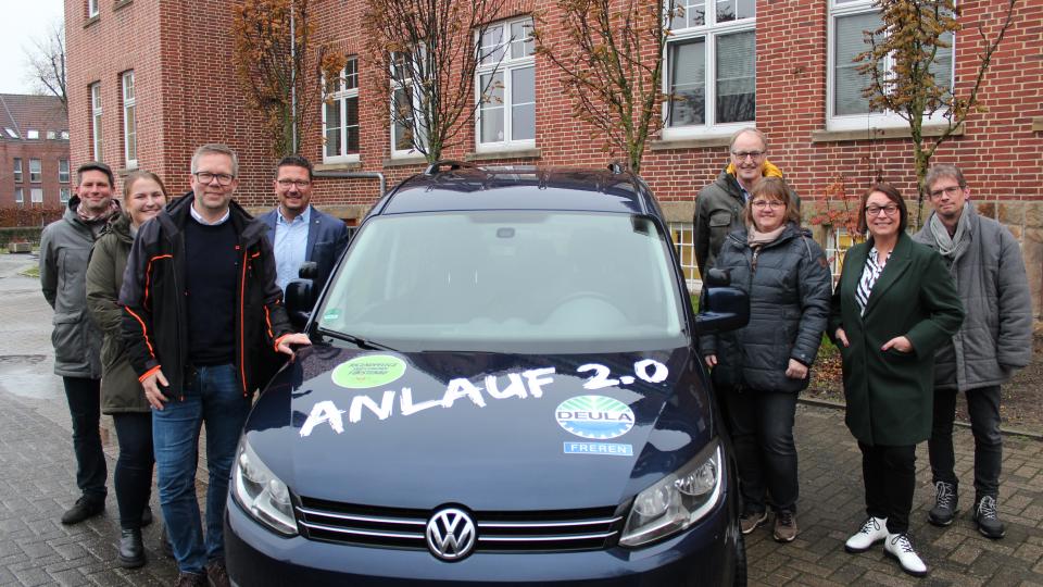 Auto mit Schriftzug Anlauf 2.0 und 8 Menschen drum herum 